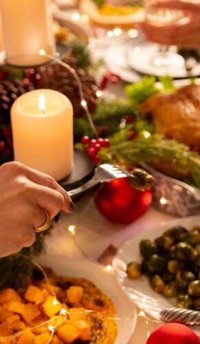 Na foto há uma mesa de jantar em que há muitos pratos, velas e pessoas comendo.