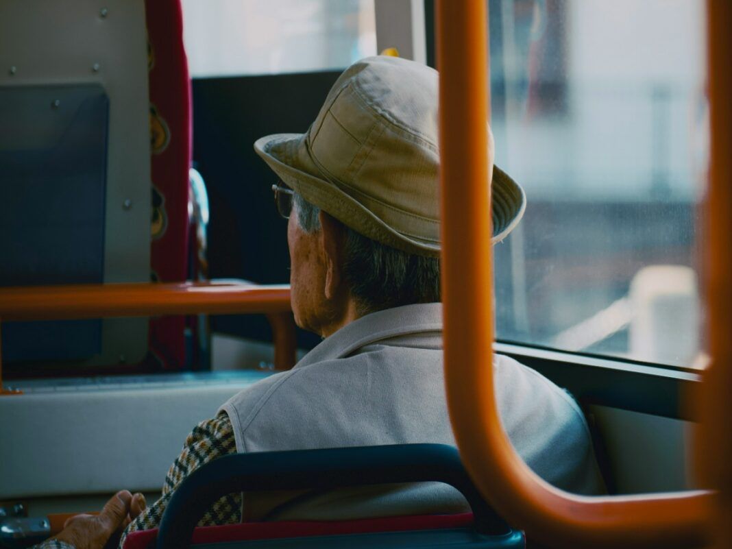 Um homem de costas sentado num ônibus, ele usa chapéu