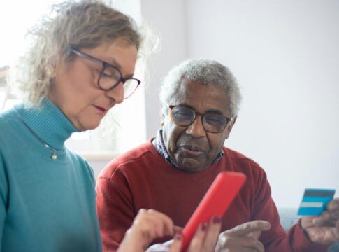 Em imagem ilustrativa, dois idosos consumindo produtos via celular