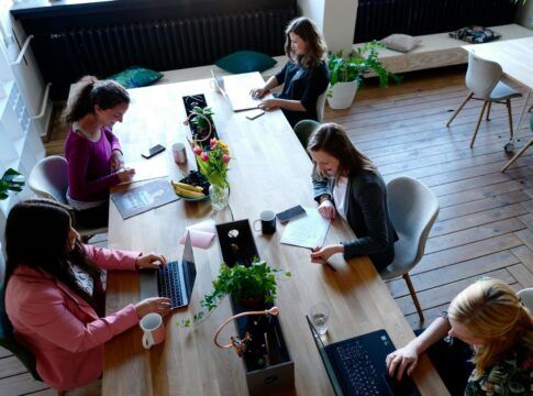 A imagem mostra um escritório com várias pessoas trabalhando numa mesa grande