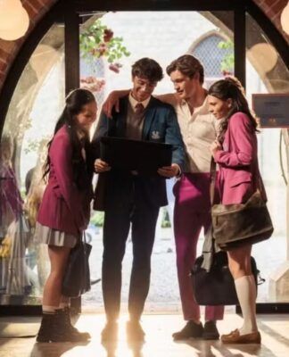 Na foto estão 4 jovens com uniformes que possuem cores cinza r osa. Eles estão em um corredor e olhando para um tablet.