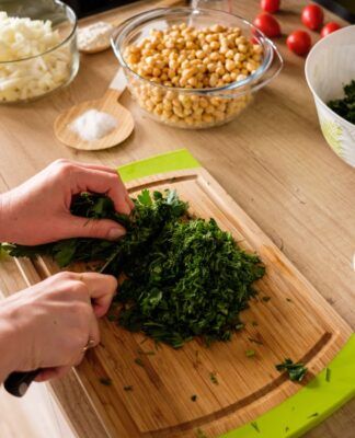 Em imagem ilustrativa, pessoa corta hortaliça vede em uma tábua de maneira