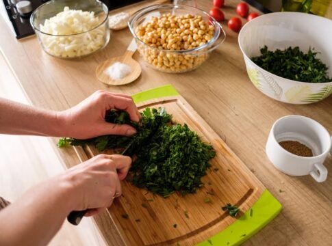 Em imagem ilustrativa, pessoa corta hortaliça vede em uma tábua de maneira