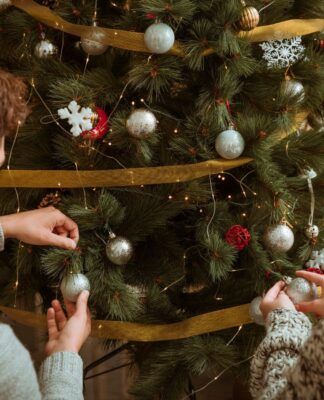 Casal colocando enfeites cinzas em uma grande árvore de Natal verde