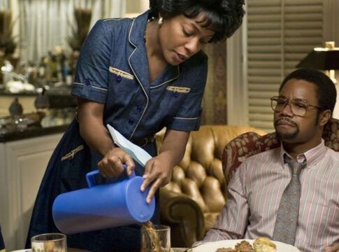 Uma mulher está de pé servindo café ao homem que está sentado na mesa.