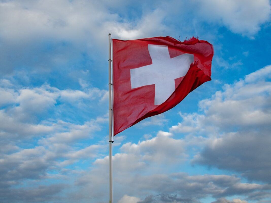 Imagem ilustrativa da bandeira da Suíça a céu aberto.
