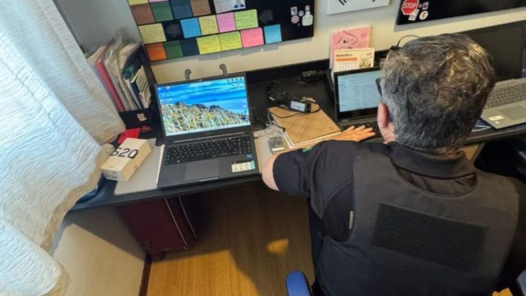 Policial acessa notebook numa escrivaninha na casa de um dos suspeitos