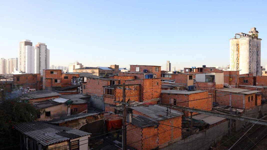 Imagem de favela no primeiro plano, com prédios de classe média ao fundo