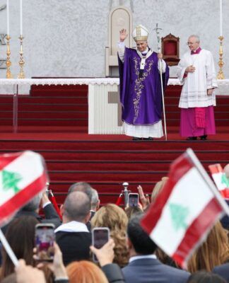 Papa Leão 14 acena aos fiéis durante missa; fiéis agitam bandeiras do Líbano