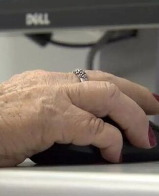 Uma mão de uma mulher idosa mexe no mouse diante de um computador