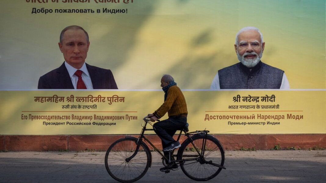 Indiano anda de bicicleta na rua à frente de um outdoor com as imagens de Putin e do primeiro-ministro indiano