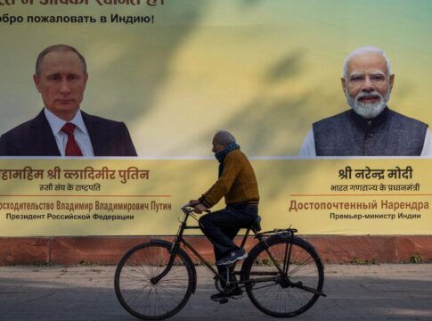 Indiano anda de bicicleta na rua à frente de um outdoor com as imagens de Putin e do primeiro-ministro indiano