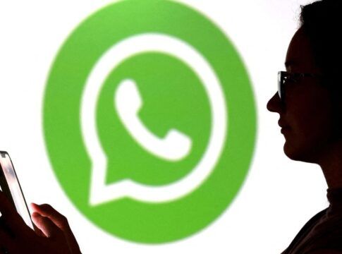 Pessoa olha para seu celular enquanto aparece o logo do Whatsapp ao fundo