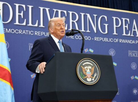 Donald Trump fala ao microfone à frente de painel onde está escrita a mensagem 