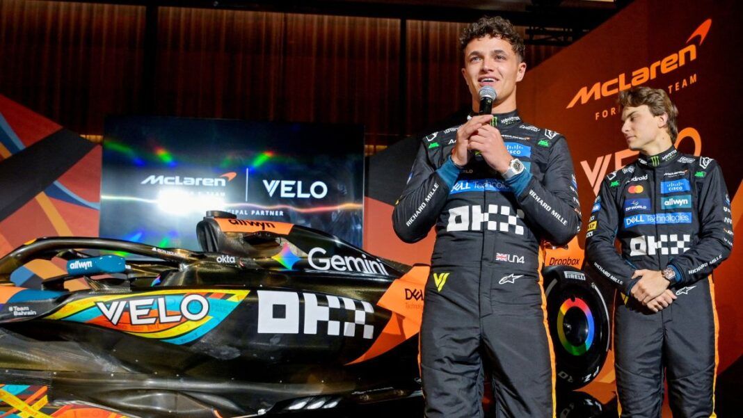 Lando Norris fala ao microfone ao lado da sua McLaren e do companheiro Oscar Piastri em evento pré-GP