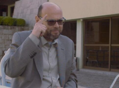 Foto de Marcelo (homem careca de terno), apontando para a cabeça durante entrevista