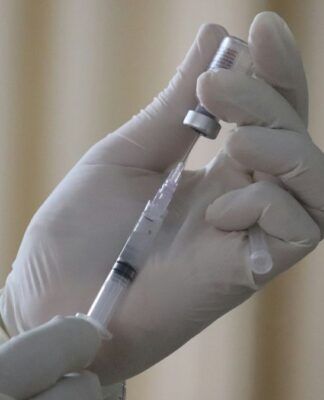 Mãos vestindo luvas de látex colocando vacina em seringa