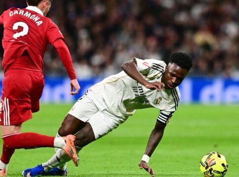 Vini Jr. está caindo no gramado após driblar jogador do Sevilla