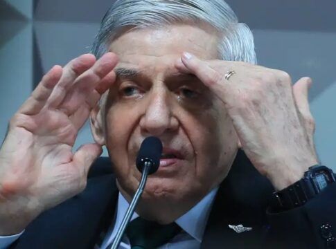 Homem de cabelos grisalhos fala ao microfone em ambiente oficial, gesticulando com as mãos próximas ao rosto enquanto usa terno escuro, camisa branca e gravata verde.