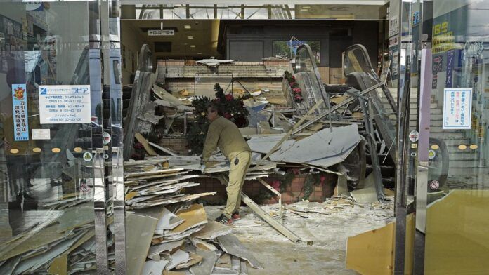 Trabalhador limpa entrada de sua loja após estrago causado por terremoto