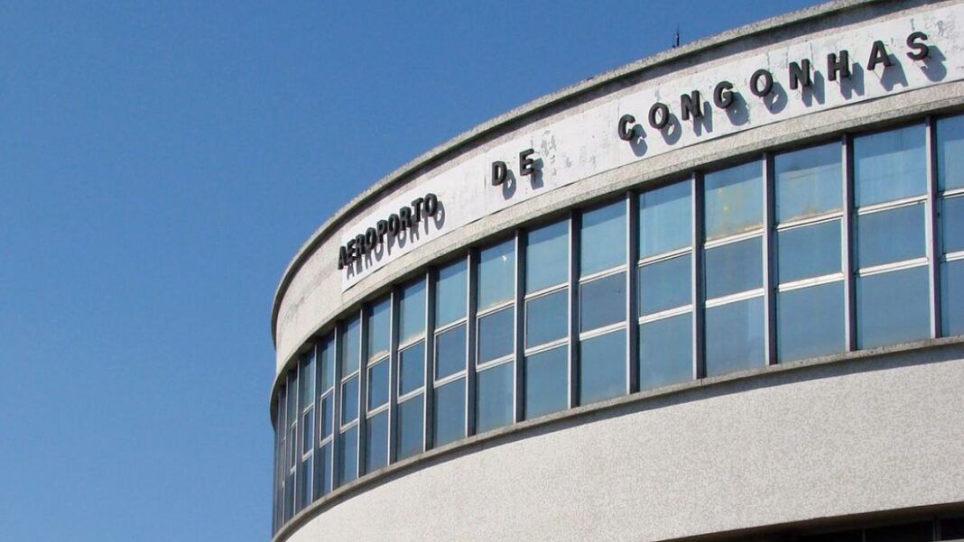 A imagem é um plano médio que foca na parte superior da fachada curva do terminal de passageiros do Aeroporto de Congonhas (CGH), em São Paulo, em um dia claro e ensolarado.