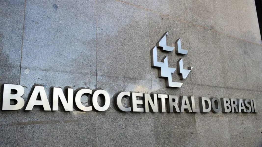 A imagem é um close-up que foca na parte central da fachada externa do edifício do Banco Central do Brasil, destacando o nome da instituição e seu símbolo em metal.