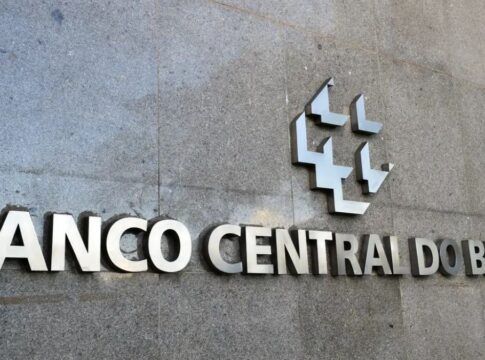A imagem é um close-up que foca na parte central da fachada externa do edifício do Banco Central do Brasil, destacando o nome da instituição e seu símbolo em metal.