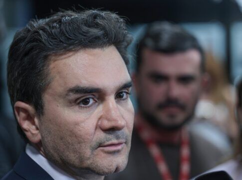 A foto é um primeiro plano (close-up) do rosto de Celso Sabino, atual Ministro do Turismo do Brasil. Ele está posicionado de três quartos, olhando para a direita da imagem com uma expressão séria e atenta, como se estivesse ouvindo uma pergunta ou concedendo uma entrevista.