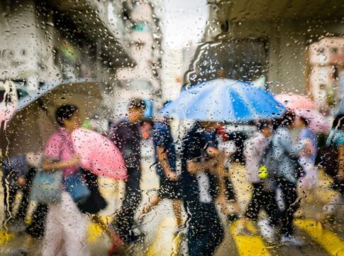 Em imagem ilustrativas, pessoas andam de guarda-chuva em tempo de chuva na rua