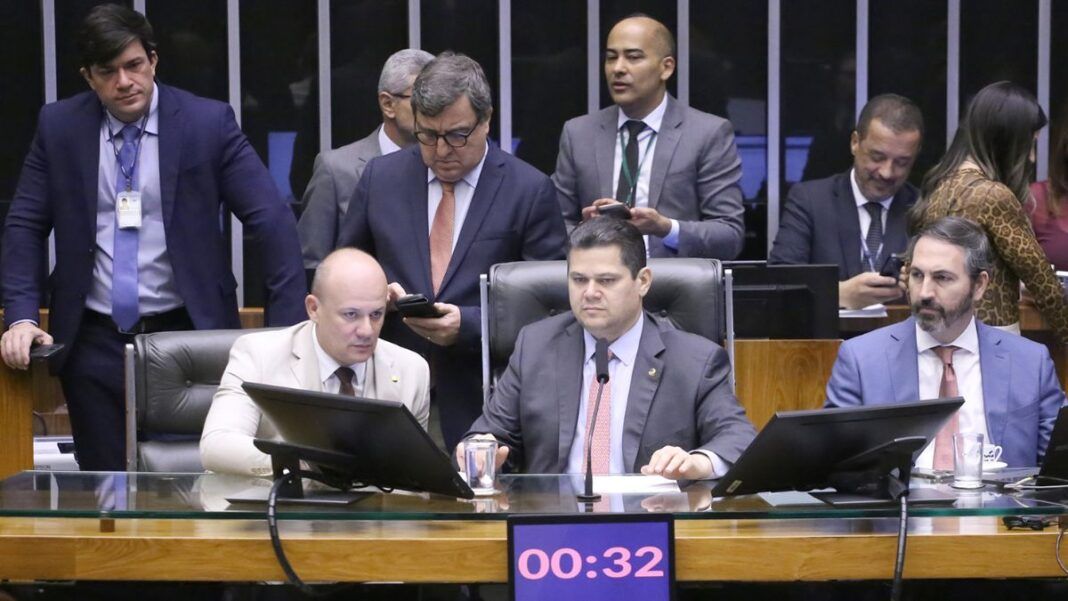 A foto mostra um grupo de parlamentares sentados e em pé, reunidos em um ambiente que se assemelha à mesa diretora ou a uma comissão dentro do Congresso Nacional .