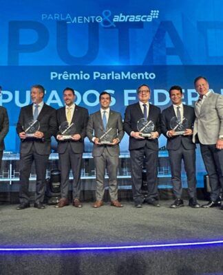 Esta é uma fotografia tirada em um evento formal de premiação, mostrando um grupo de homens, a maioria vestindo ternos escuros, em um palco.