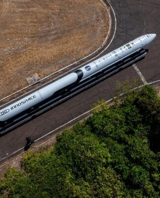Esta é uma foto aérea (tirada de cima) que mostra um foguete sendo transportado por uma estrada ou pista em uma área predominantemente rural ou de vegetação.