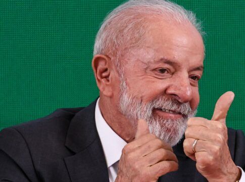 A foto mostra um plano médio do presidente Luiz Inácio Lula da Silva, que está sorrindo e gesticulando com as duas mãos em um sinal de aprovação (