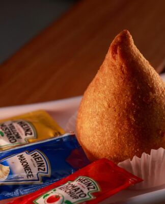 Uma coxinha em cima de uma mesa com saches de molhos ao lado