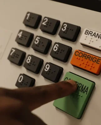 urna eletrônica de votação com foco nos botões em especial um dedo indicador apertando o botão verde