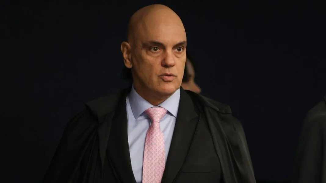 A imagem é um plano médio que foca no ministro do Supremo Tribunal Federal (STF), Alexandre de Moraes, em um ambiente interno e formal.