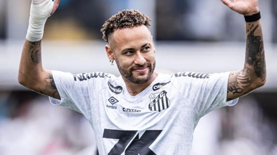 A imagem é um plano médio do jogador de futebol Neymar Jr., vestindo a camisa do Santos Futebol Clube, em um momento de interação com o público ou torcida.