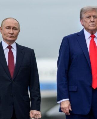 A imagem é um plano médio que captura os presidentes Vladimir Putin e Donald Trump lado a lado, em pé, em um ambiente externo que se assemelha a uma pista de aeroporto ou área externa de recepção, sob um céu nublado.