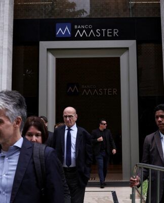 Um segurança segura uma grade enquanto pessoas deixam o Banco Master após a prisão do acionista controlador da instituição, Daniel Vorcaro