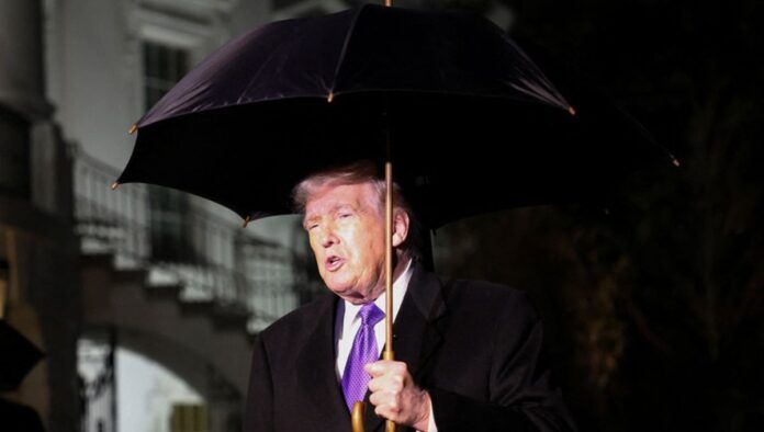 O presidente dos Estados Unidos, Donald Trump, segura um guarda-chuva enquanto fala com jornalistas ao deixar a Casa Branca com destino à Flórida