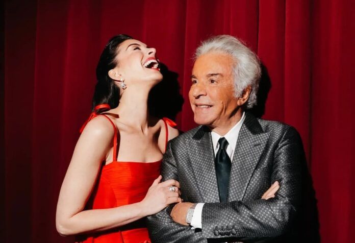 Anne Hathaway ao lado de Valentino Garavani, usando vestido vermelho da marca do estilista