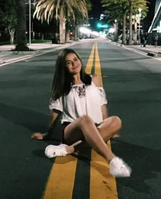 Foto de Maisa há dez ano sentada em uma rua com palmeiras na calçada