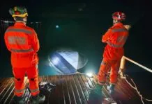 Dois profissionais do Corpo de Bombeiros observam lancha afundada