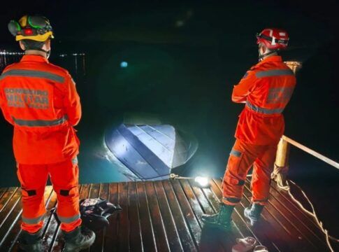 Dois profissionais do Corpo de Bombeiros observam lancha afundada