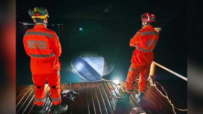 Dois profissionais do Corpo de Bombeiros observam lancha afundada