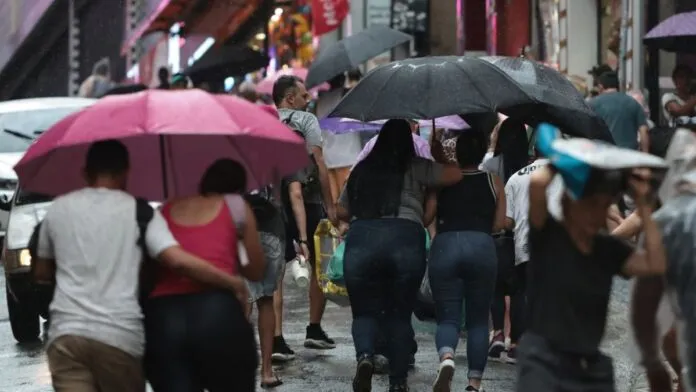 Pessoas caminhando na rua sob chuva e com guarda-chuva