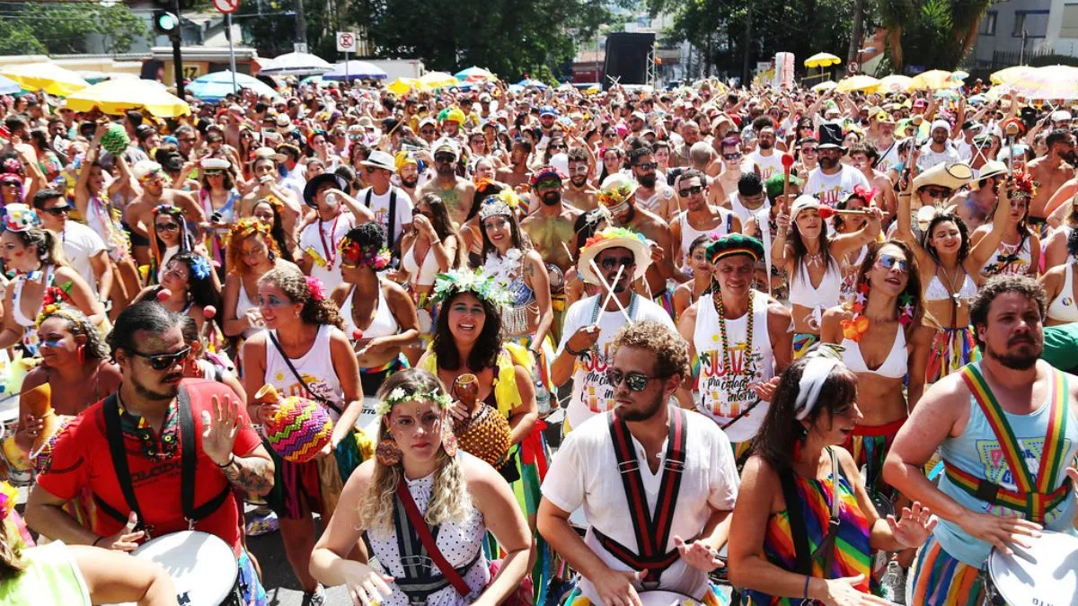 Pessoas tocando na bateria de um bloco de carnaval em BH, todos de branco, durante o dia