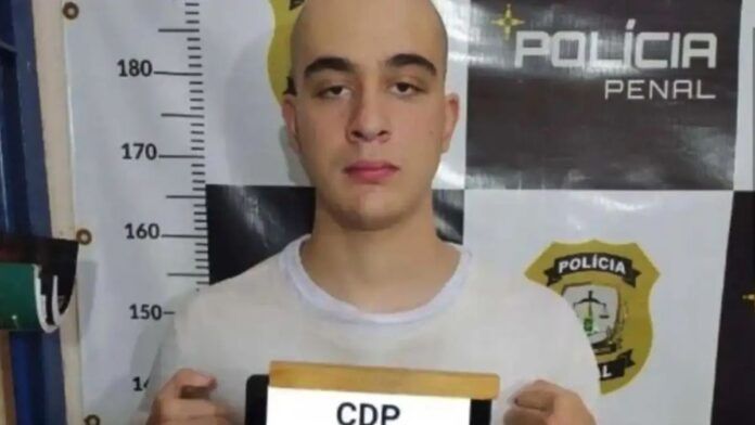 Piloto Pedro Turra é fotografado na delegacia enquanto segura placa com seu número de identificação