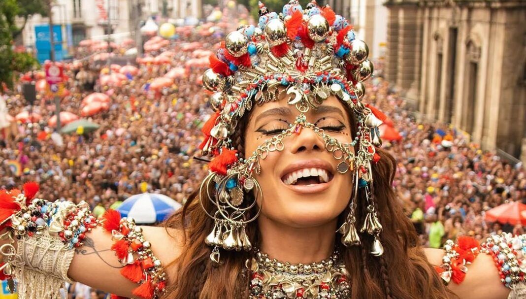 Anitta de olhos fechados e fantasiada de orixá em cima do bloco, com multidão atrás