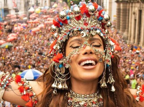 Anitta de olhos fechados e fantasiada de orixá em cima do bloco, com multidão atrás